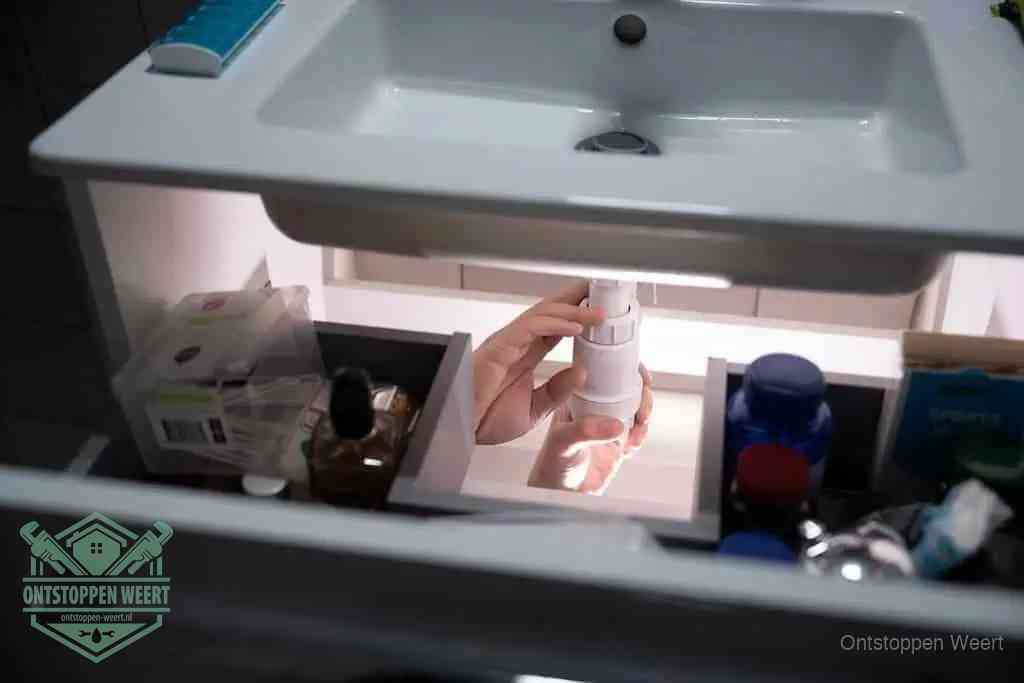Een pompfles met zeep boven een wastafel, de heet water en afwasmiddel-methode om een vetprop in de afvoer los te maken in Weert