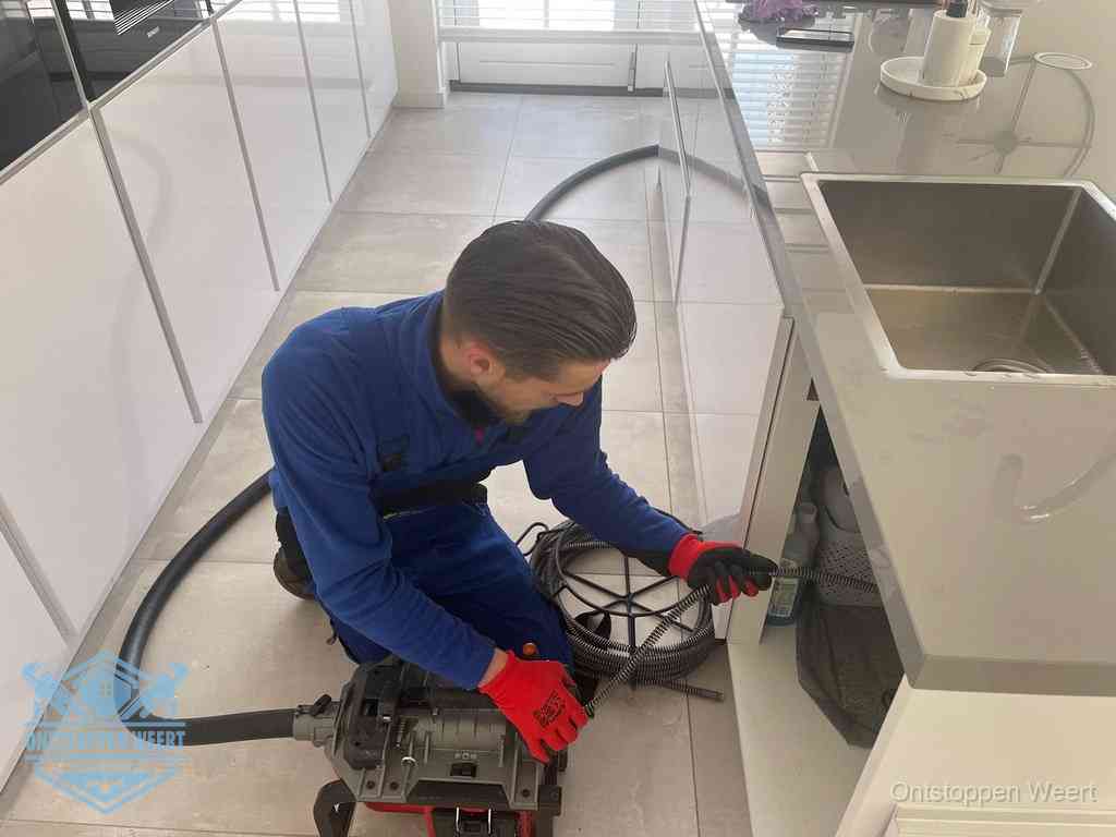 Een monteur ontstopt de keukenafvoer onder de spoelbak met een elektrische veermachine in Weert