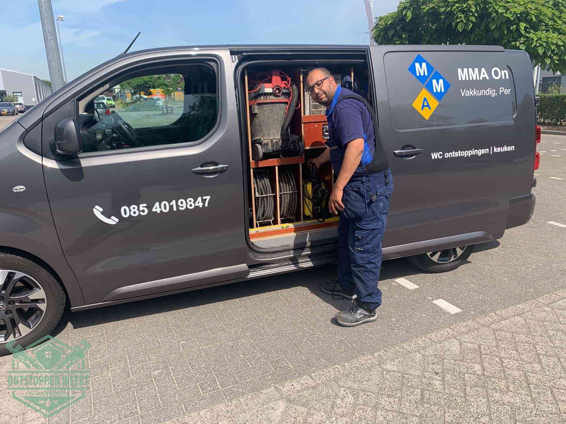 Een monteur bij de open schuifdeur van zijn bedrijfsbus op een parkeerplaats, klaar om de oorzaak van terugkerende afvoerverstoppingen aan te pakken in Weert