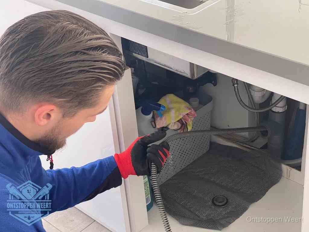 Een monteur voert een flexibele ontstoppingsveer in de afvoer om een verstopping voorbij de bocht van het toilet te bereiken in Weert