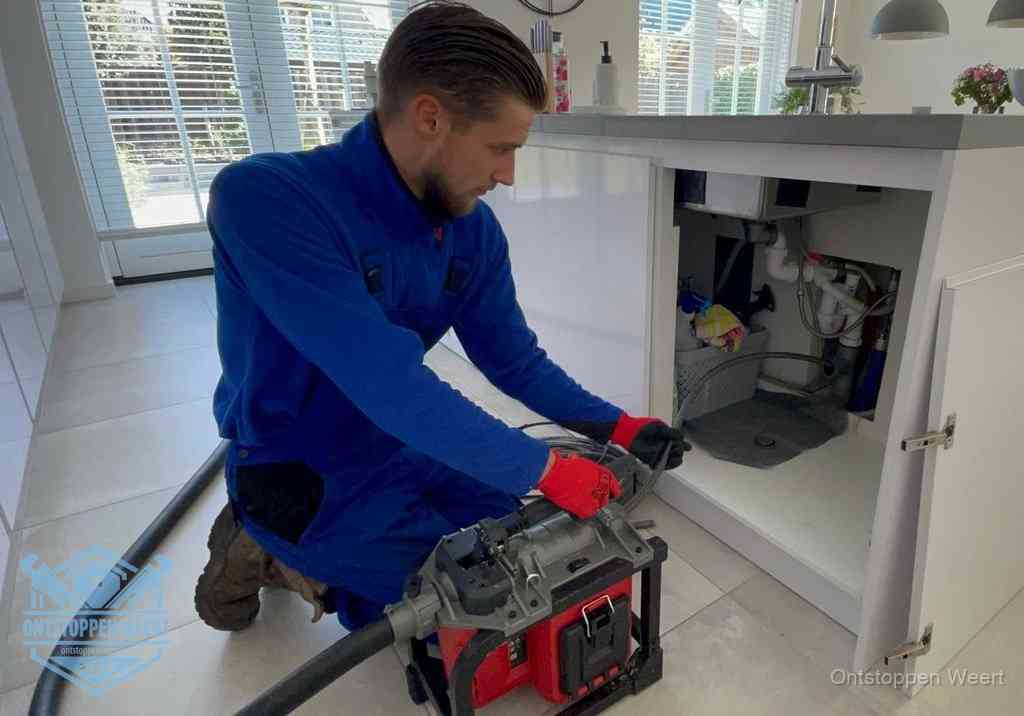Een monteur voert een professionele elektrische ontstoppingsmachine in de afvoer onder de spoelbak tijdens het gootsteen ontstoppen in Weert